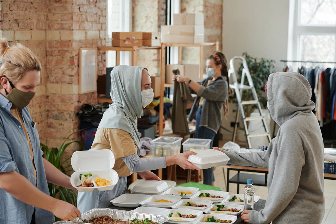 Volunteers wearing face masks distribute food in takeaway boxes at a community charity event.