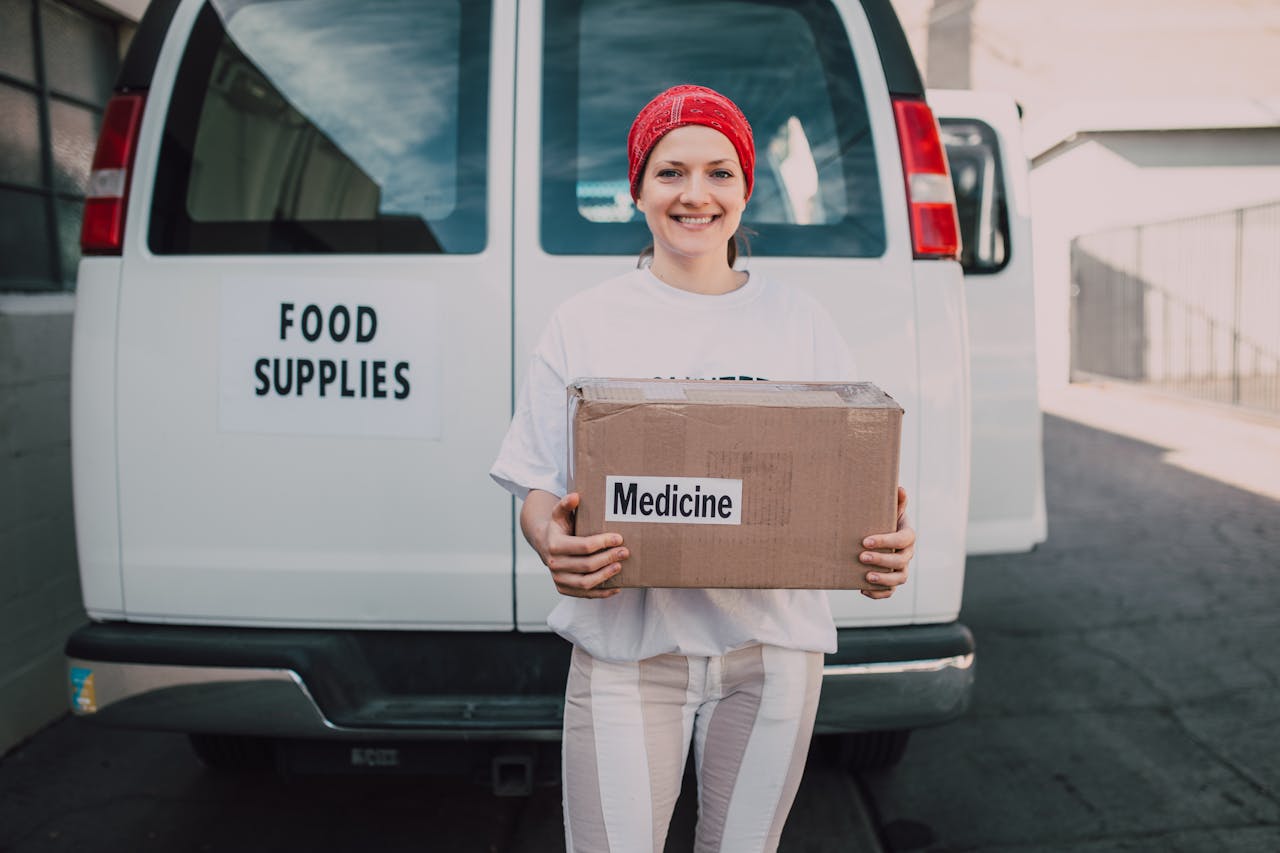 A cheerful volunteer stands with a medicine box in front of a food supplies van.